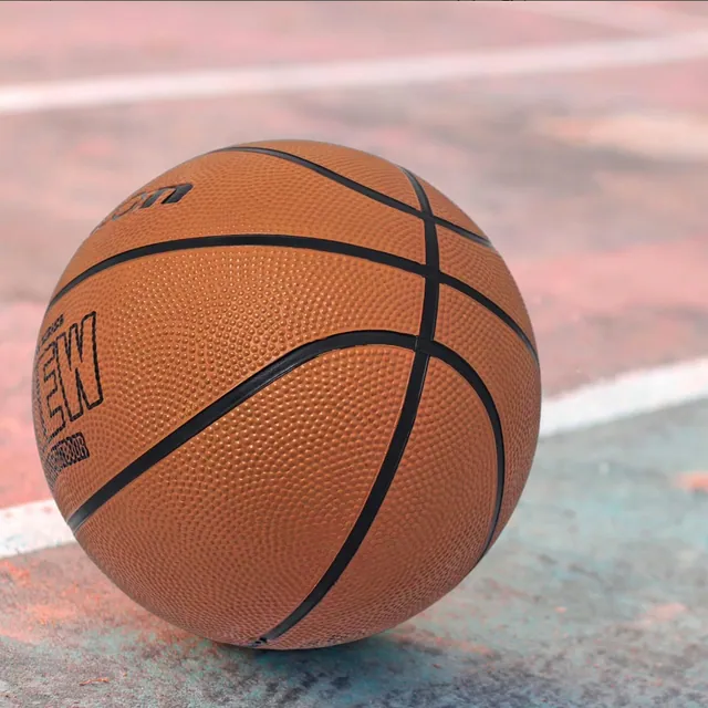 An orange rubber basketball resting on an outdoor court beside a painted line
