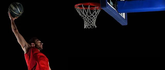 A player in a red jersey leaping toward the hoop with a basketball