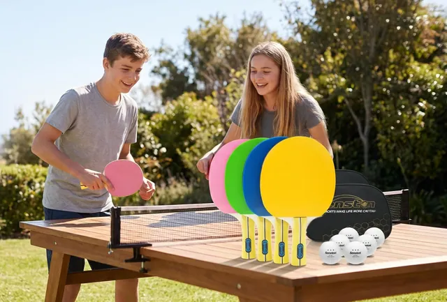 A teenage boy and girl playing table tennis on a wooden table in a sunny backyard