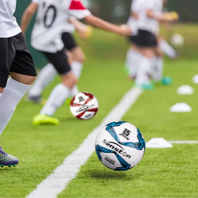 Youth players in white kits doing drills while a white and blue ball rolls past the cones
