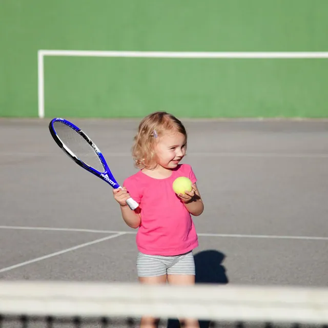 A toddler holding a junior tennis racket and a ball on a court