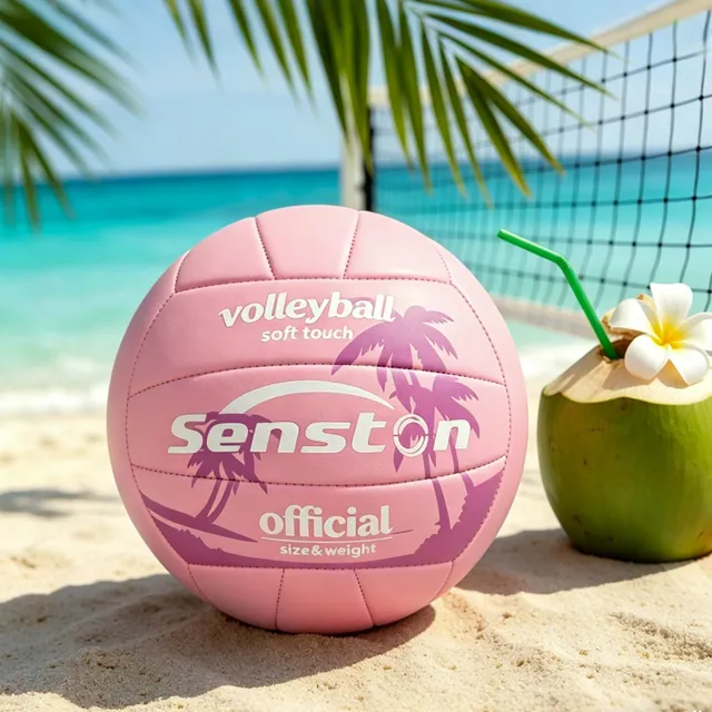 A pink palm-print volleyball on the sand next to a coconut drink