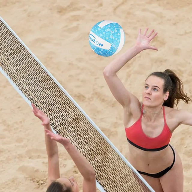 A woman spiking a blue star-print volleyball over a beach net